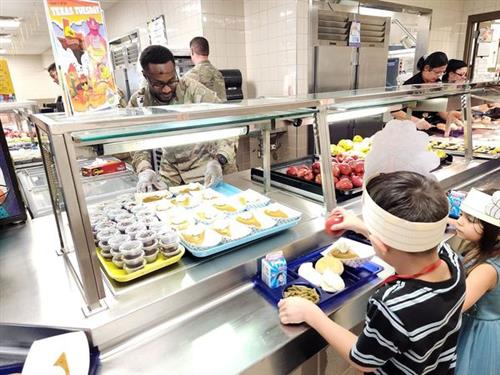 students in lunch line served by soldier