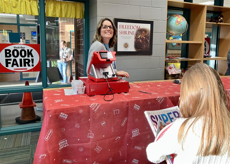 Flick is helping a student buy a book at the 2023 Spring Book Fair